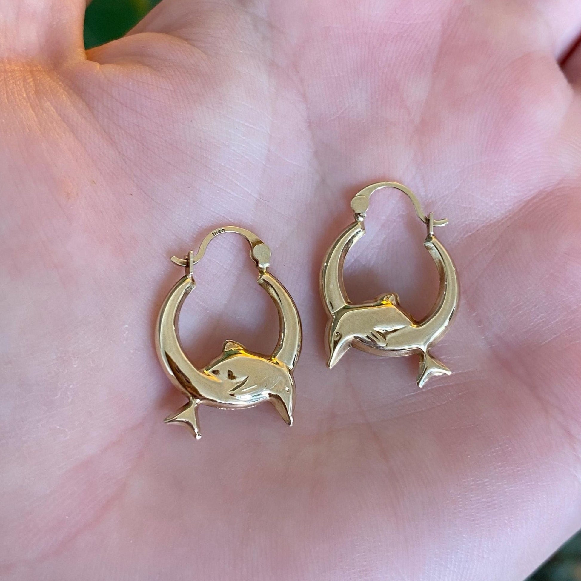 Gold dolphin earrings held in a hand with a blurred background