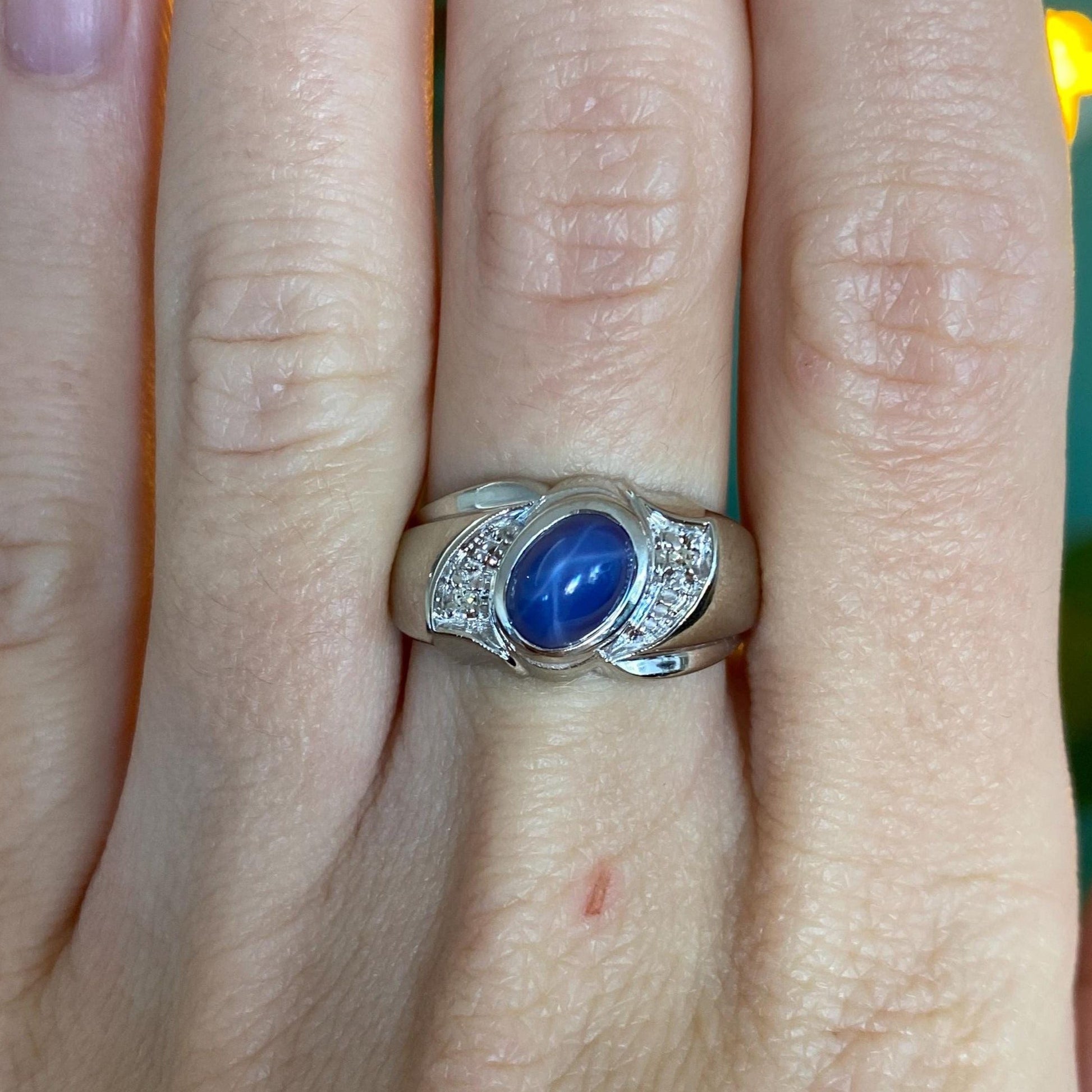 Silver ring with a blue stone on a finger against a neutral background