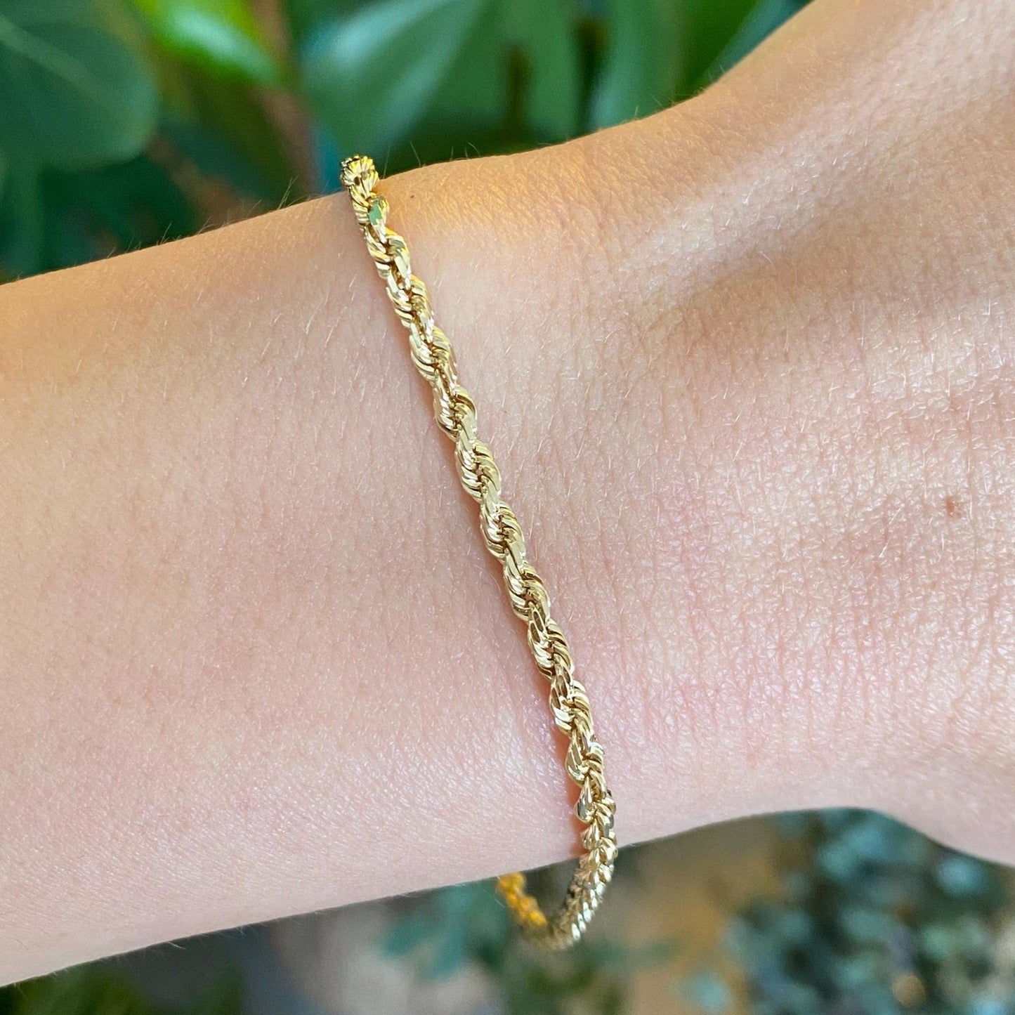 Gold bracelet on a wrist with a blurred green leafy background